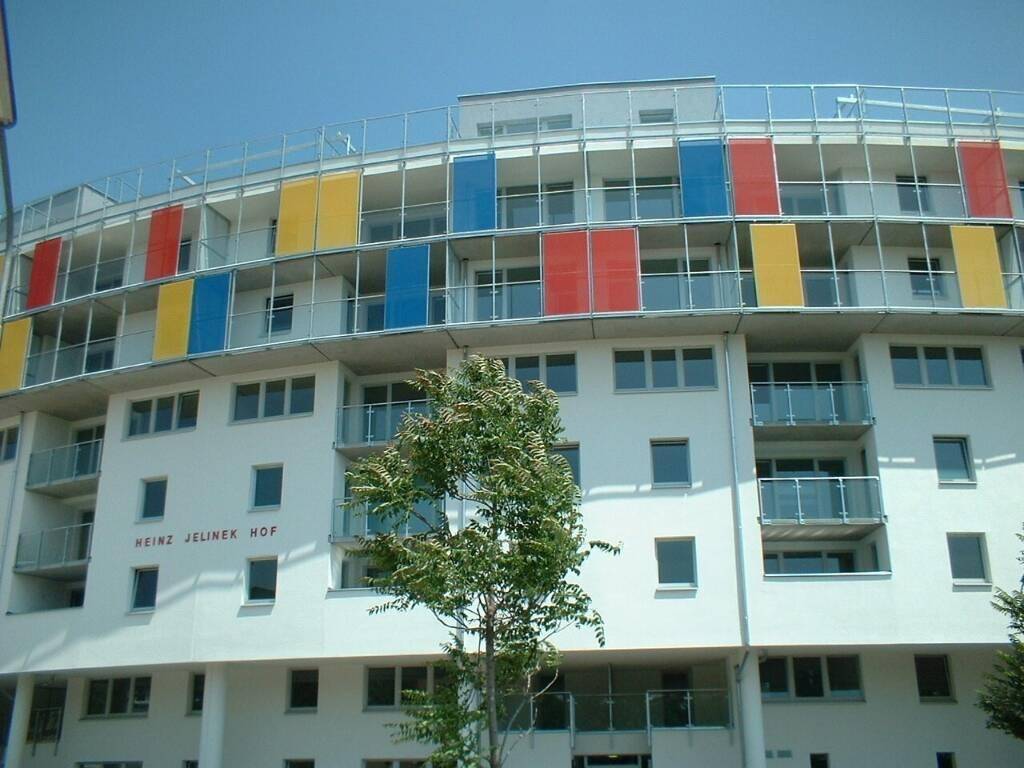 Moderne Gebäudefassade mit runder Form, farbigen Paneelen und zahlreichen Balkonen.