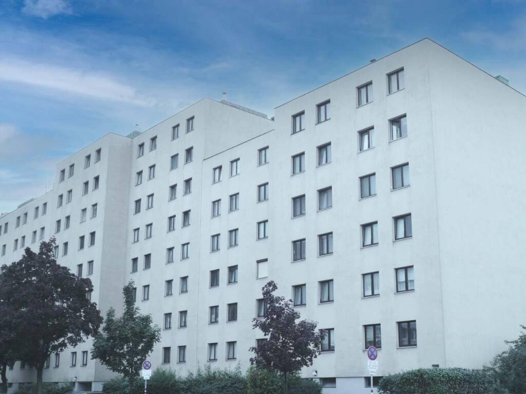 Lange Fassade eines modernen Wohngebäudes mit vielen Fenstern unter einem leicht bewölkten Himmel.