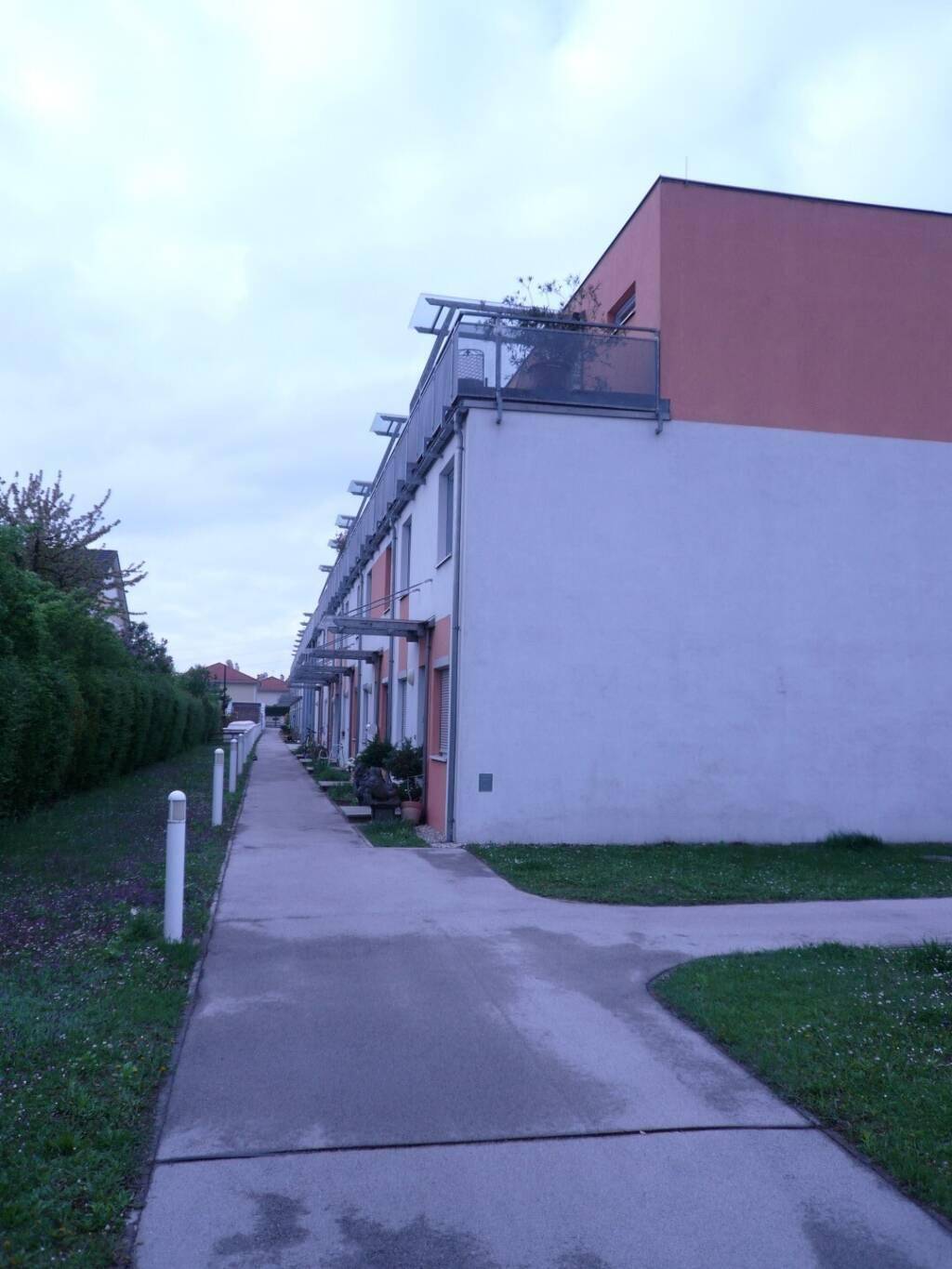 Reihenhausanlage mit modernen Fassaden, Balkonen und einem gepflasterten Gehweg.
