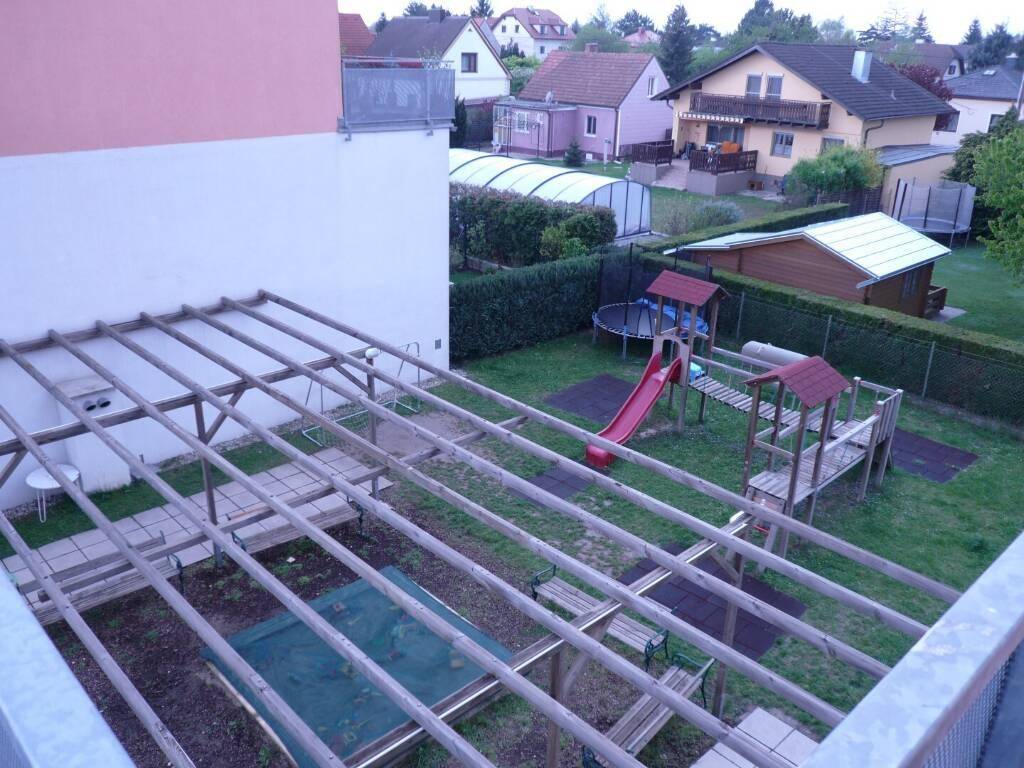 Gartenbereich mit Holzpergola, Kinderspielplatz und Trampolin, umgeben von weiteren Häusern.