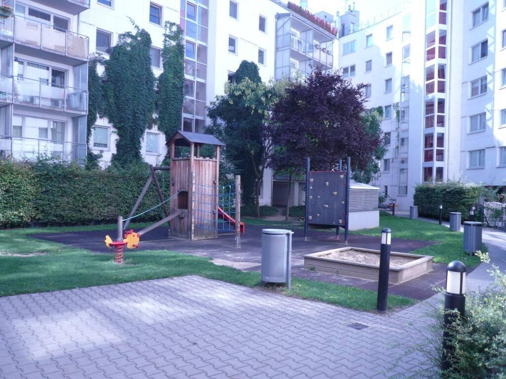 Kinderspielplatz mit Sandkasten und Klettergerüst, umgeben von Wohngebäuden und Grünflächen.