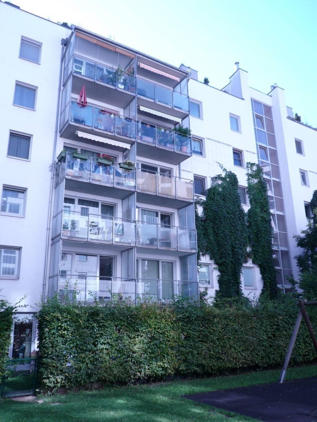 Wohngebäude mit mehreren Balkonen und üppigem Grün an der Fassade, gesehen von einem Spielplatz.