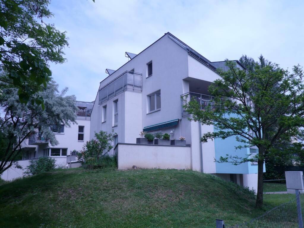 Moderne Wohnanlage mit Balkonen, Photovoltaikanlage auf dem Dach und umgebender Grünfläche.