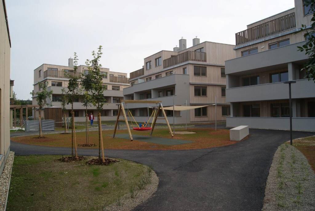 Moderne Wohnanlage mit mehreren Gebäuden, einem Gemeinschaftsgarten, Spielplatz und jungen Bäumen.