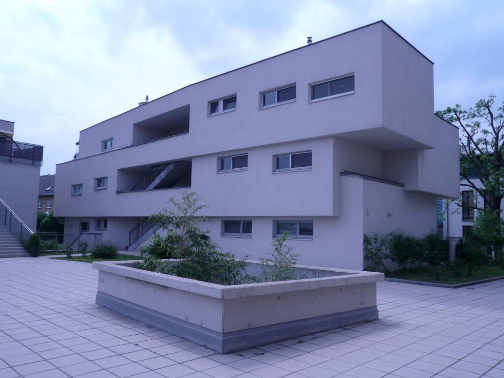 Zeitgenössisches Gebäude mit klaren Linien, Flachdach und einem gepflasterten Innenhof mit Pflanzkübel.