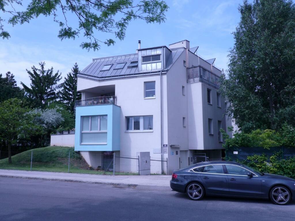 Modernes Wohnhaus mit Mansarddach, Balkon und hellblauer Fassadenakzentuierung an der Straße.