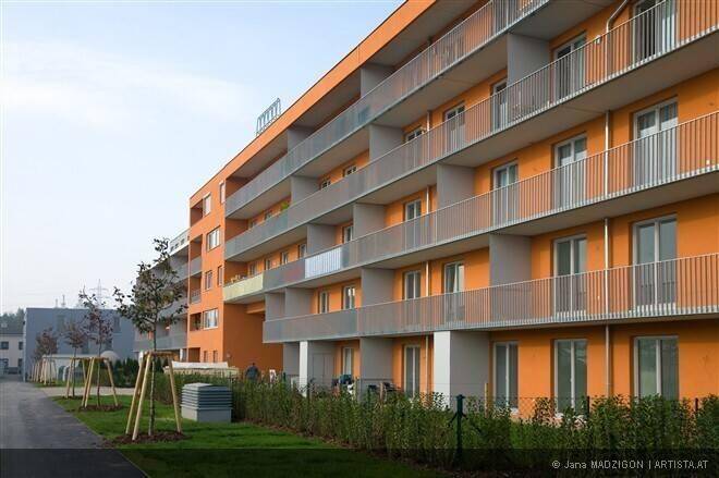 Ansicht eines modernen Apartmentkomplexes mit orangefarbenen Fassaden, Balkonen und einer begrünten Außenanlage.