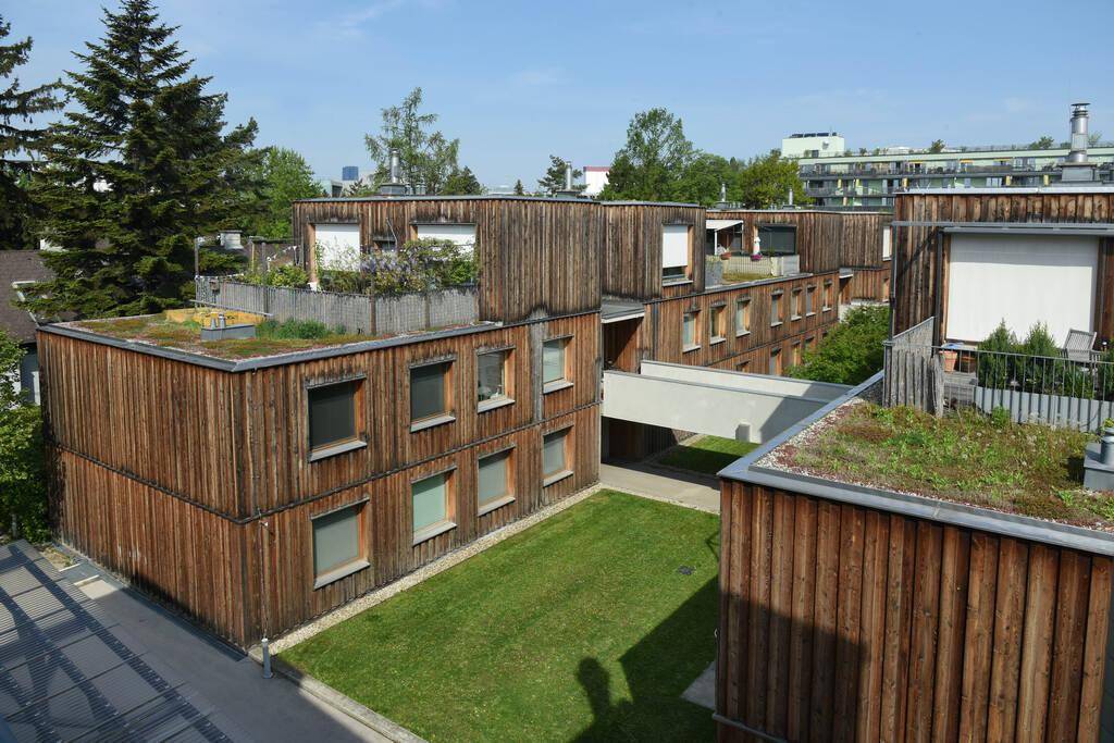 Mehrere moderne Gebäude mit Holzfassaden, begrünten Flachdächern und einem grünen Innenhof.