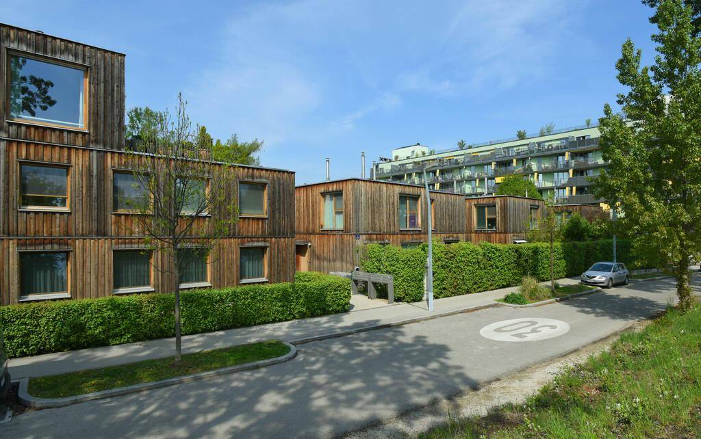 Moderne Wohngebäude mit Holzfassaden, grünen Hecken und einer ruhigen Straße in einer Wohnsiedlung.