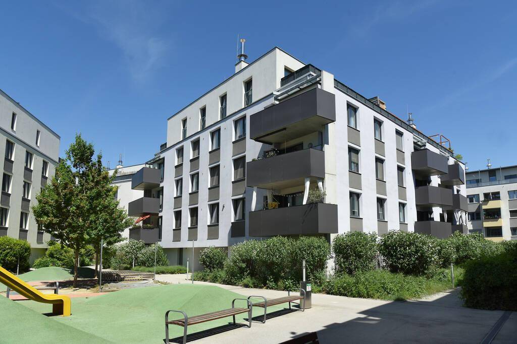 Modernes Wohngebäude mit Balkonen, umgeben von einem grünen Innenhof mit Spielplatz und Sitzgelegenheiten.