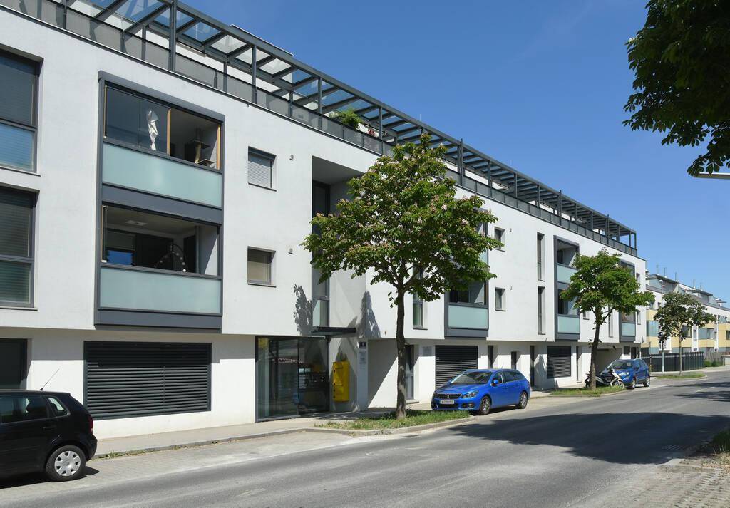 Zeitgenössisches Wohngebäude mit großen Fenstern, Balkonen und einer Dachterrasse entlang der Straße.