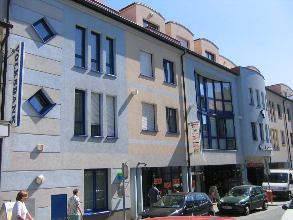 Modernes mehrstöckiges Gebäude mit blauer und beiger Fassade, großen Fenstern und einem Volksbank-Schild an einer belebten Straße.