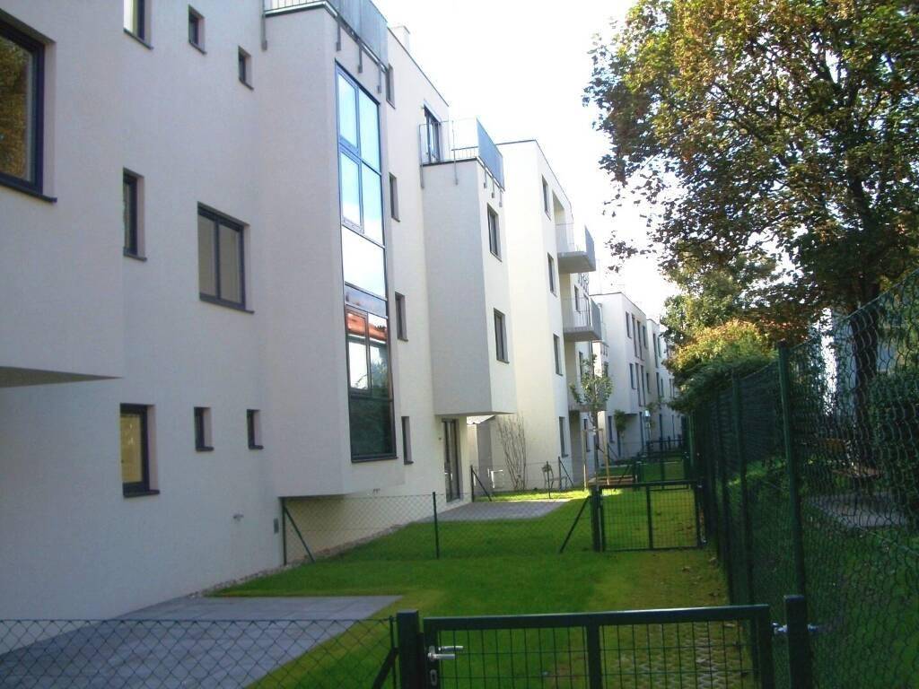 Moderne Wohnanlage mit weißer Fassade, großen Fenstern, Balkonen und kleinen Gärten.