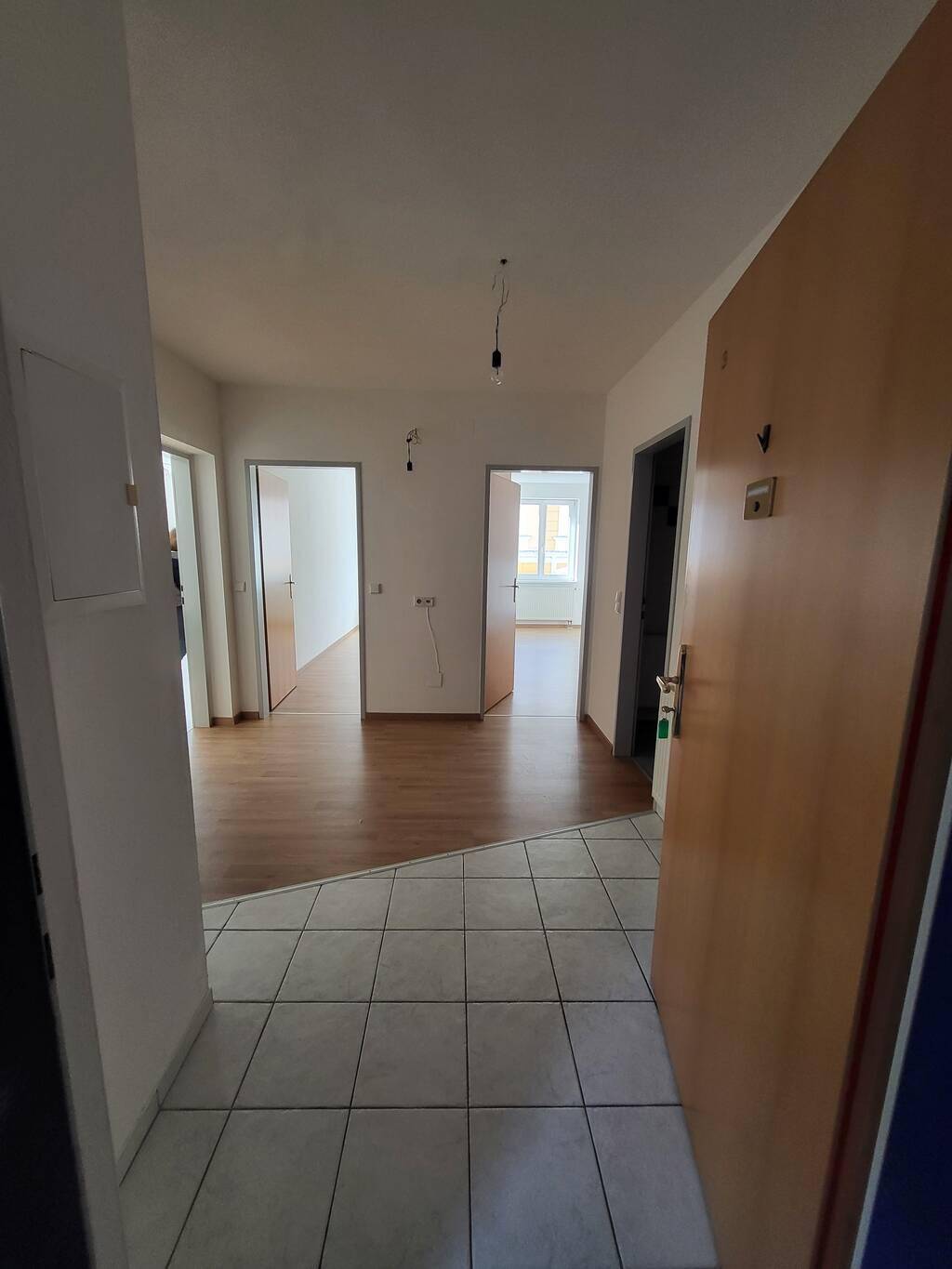 Eingangsbereich mit Fliesenboden, der in Laminat übergeht, und Blick in angrenzende Zimmer.
