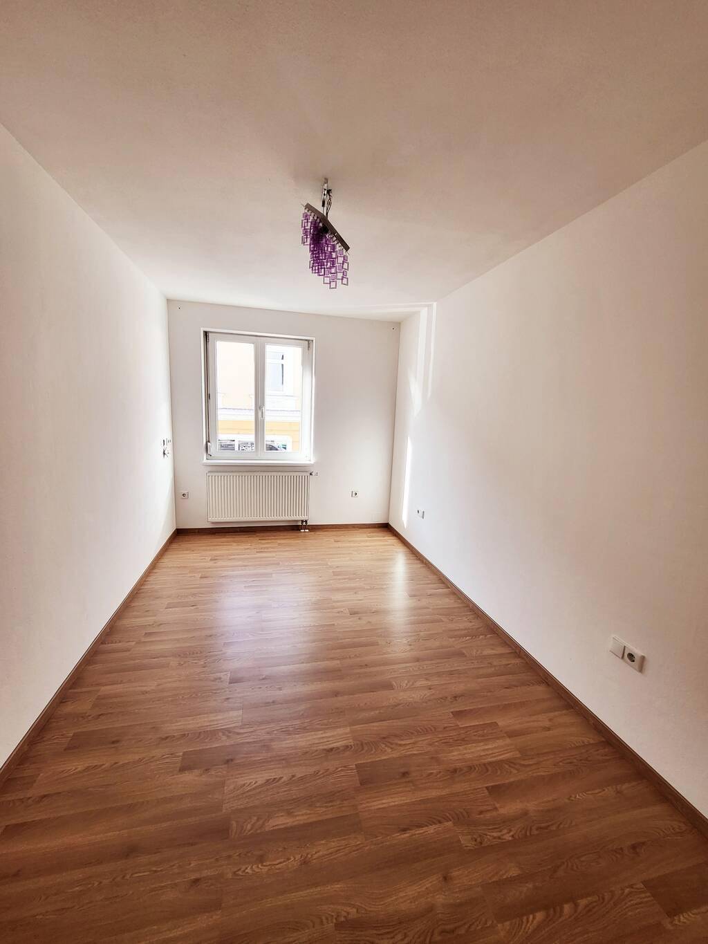 Helles, leeres Zimmer mit Laminatboden und einem Fenster, bereit zur individuellen Gestaltung.