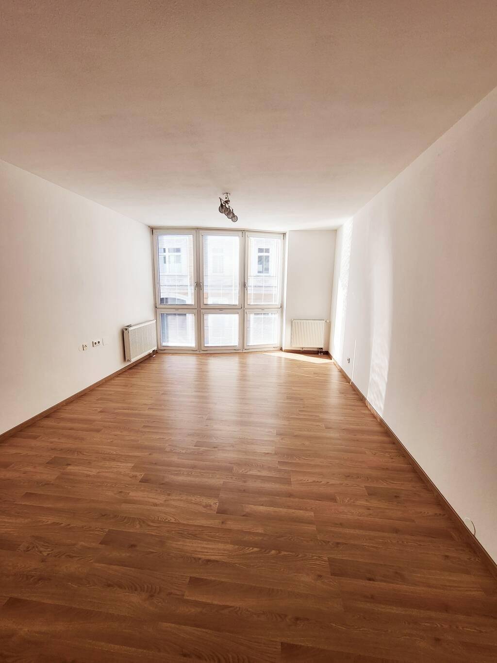 Geräumiges, helles Zimmer mit Laminatboden und großen Fenstern, die viel Licht spenden.