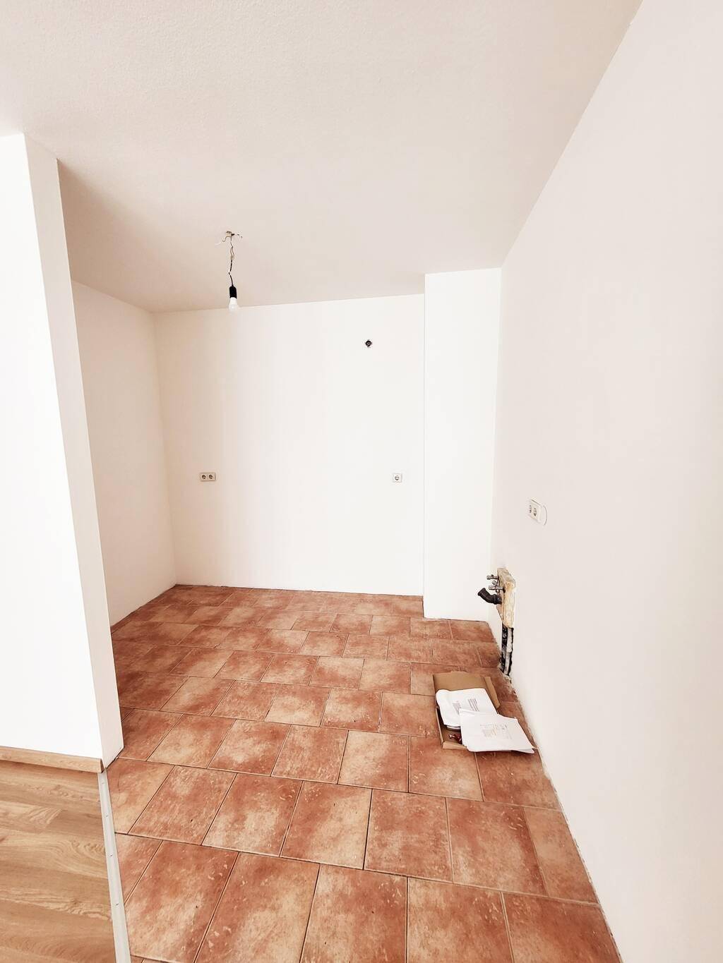 Leerer Küchenbereich mit Terrakotta-Fliesenboden und Anschlüssen für eine zukünftige Einbauküche.