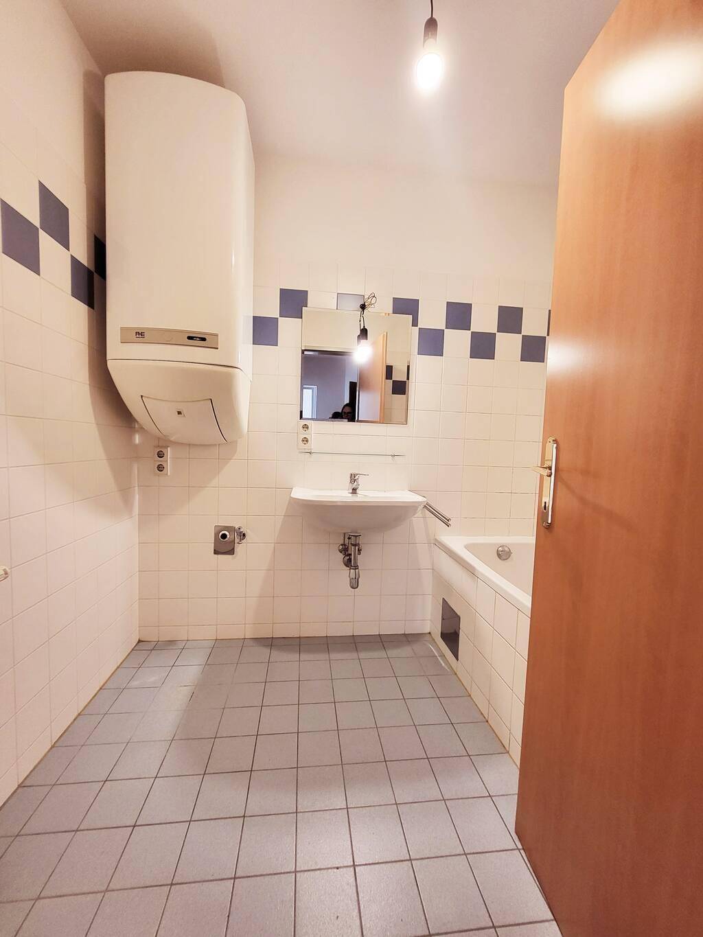 Badezimmer mit Badewanne, Waschbecken und Boiler, ausgestattet mit blau-weißen Fliesen.