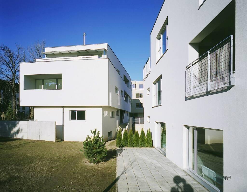 Helle, moderne Wohngebäude mit großen Fenstern, Balkonen und einer gepflegten Rasenfläche.