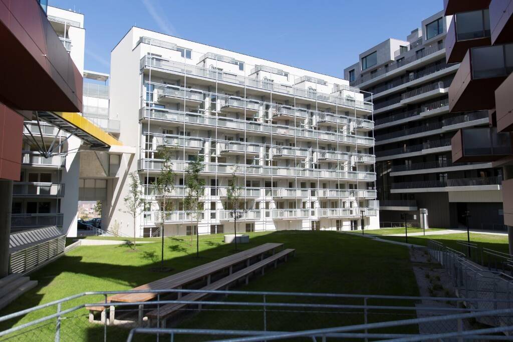 Modernes weißes Apartmentgebäude mit zahlreichen Balkonen und gepflegter Grünanlage.