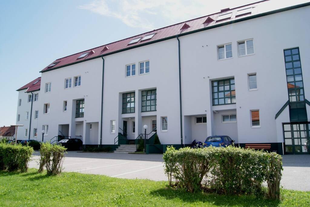 Moderne Reihenhäuser mit weißer Fassade, rotem Satteldach und gepflegter Grünanlage mit Parkplätzen.