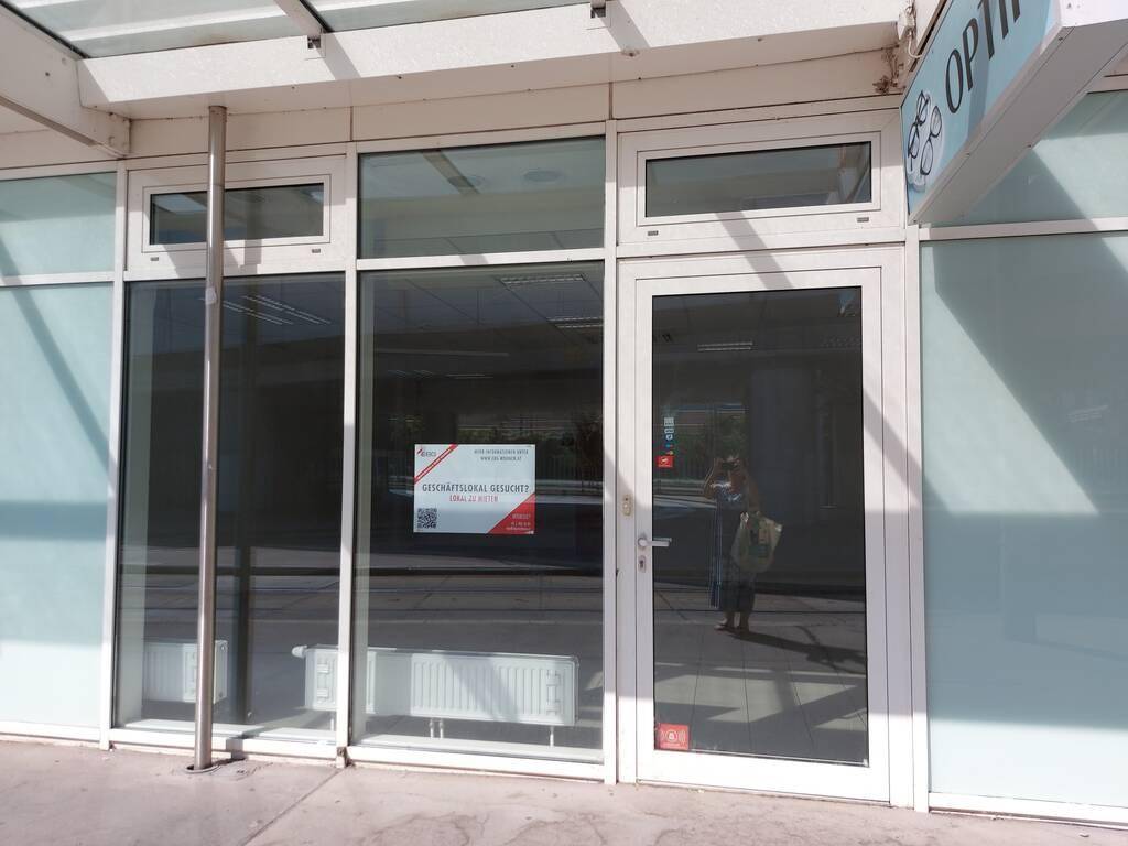 Eingangsbereich eines Geschäfts mit großen Glasfenstern und einer Werbetafel an der Fassade.