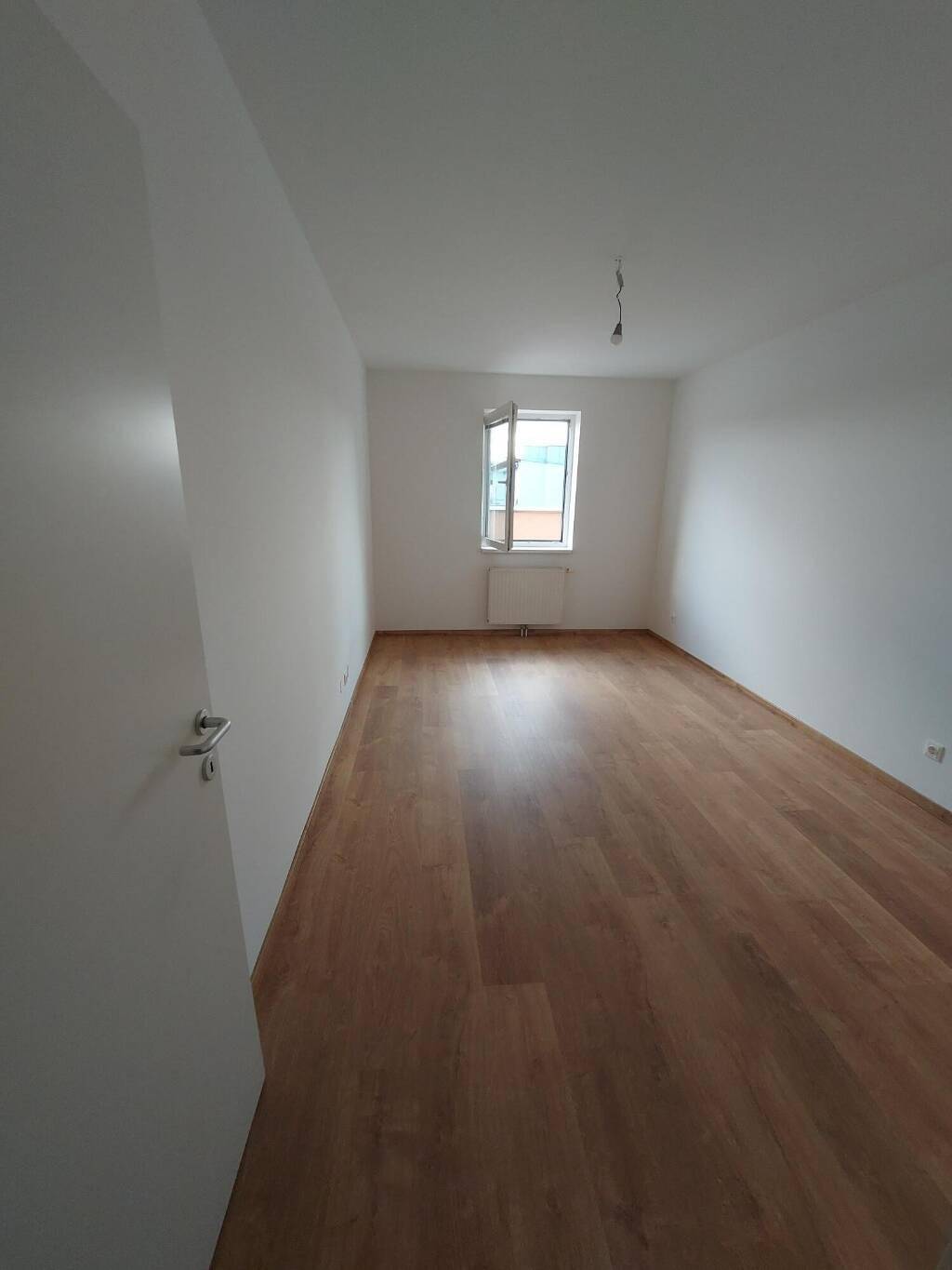 Helles, leeres Zimmer mit Laminatboden und einem Fenster, bereit zur individuellen Gestaltung.
