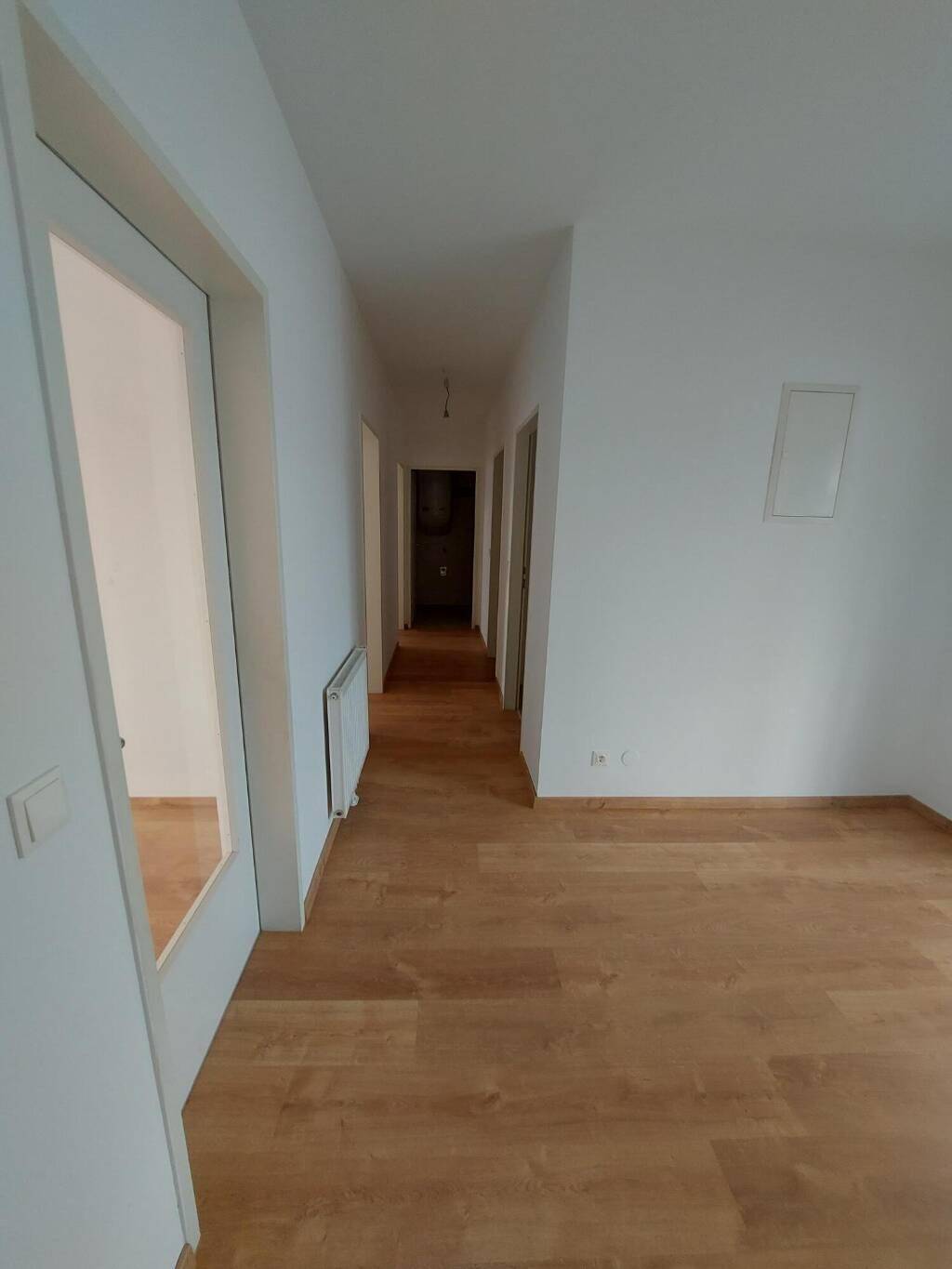 Langer, heller Flur mit Laminatboden und weißen Wänden, der zu verschiedenen Zimmern führt.