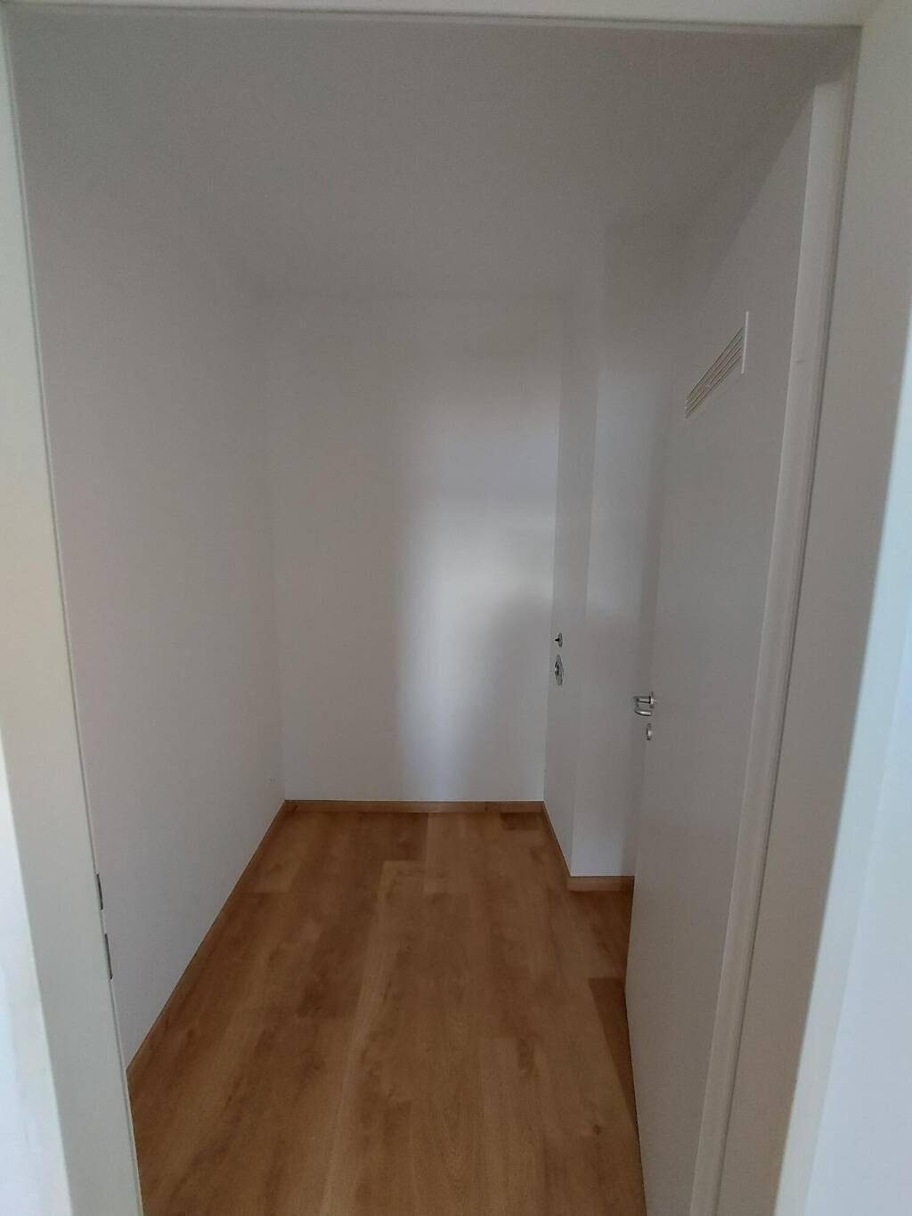 Kleiner, leerer Raum mit Laminatboden und weißen Wänden, ideal als Abstellraum oder begehbarer Kleiderschrank.
