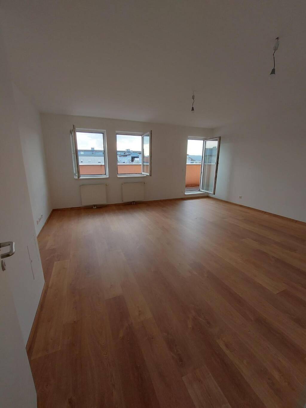 Geräumiges, helles Wohnzimmer mit Laminatboden, großen Fenstern und Zugang zu einem Balkon.