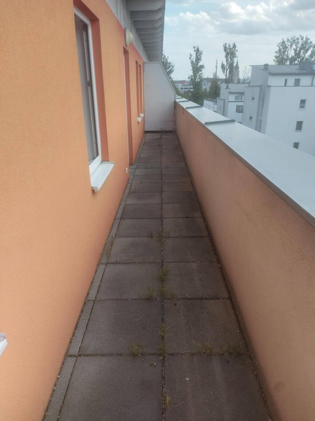 Langer, schmaler Balkon mit Fliesenboden und Blick auf die umliegenden Gebäude.