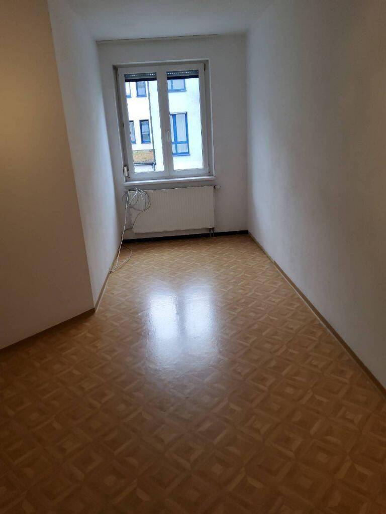 Leeres Schlafzimmer mit Parkettboden, einem Fenster und Heizkörper unter dem Fenster.