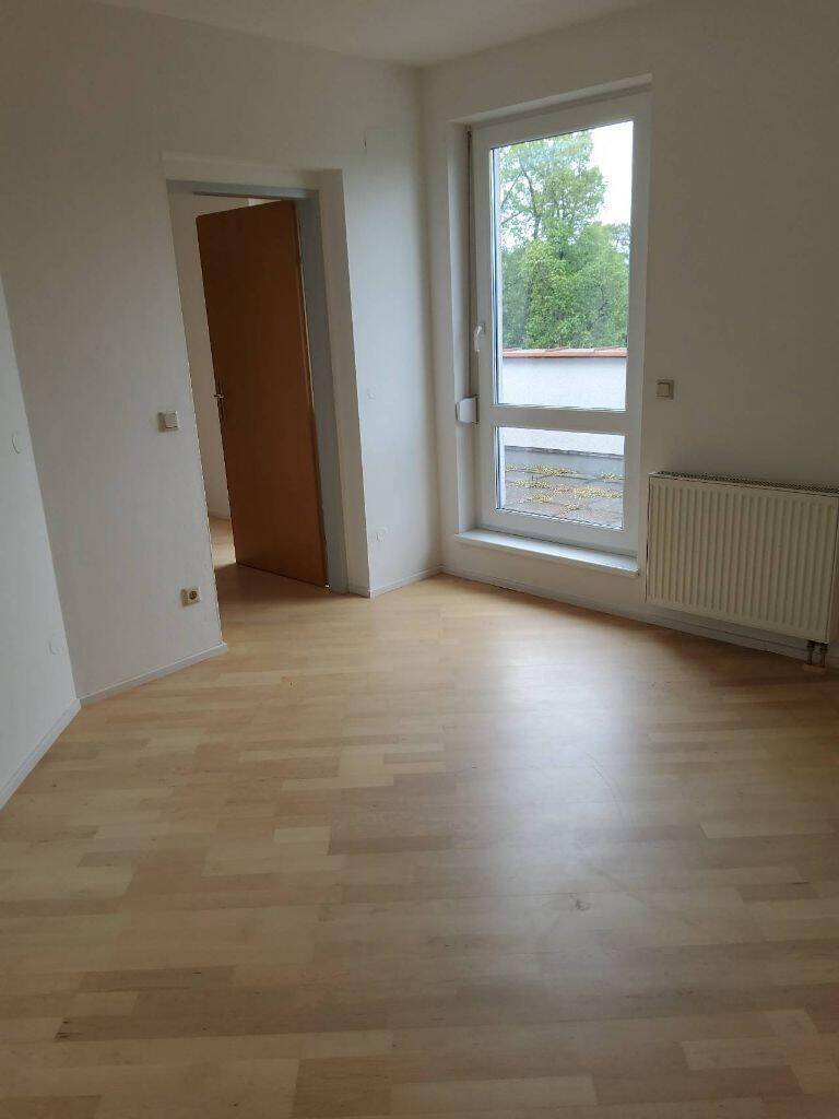 Helles Schlafzimmer mit hellem Holzboden, großem Fenster und Heizkörper.