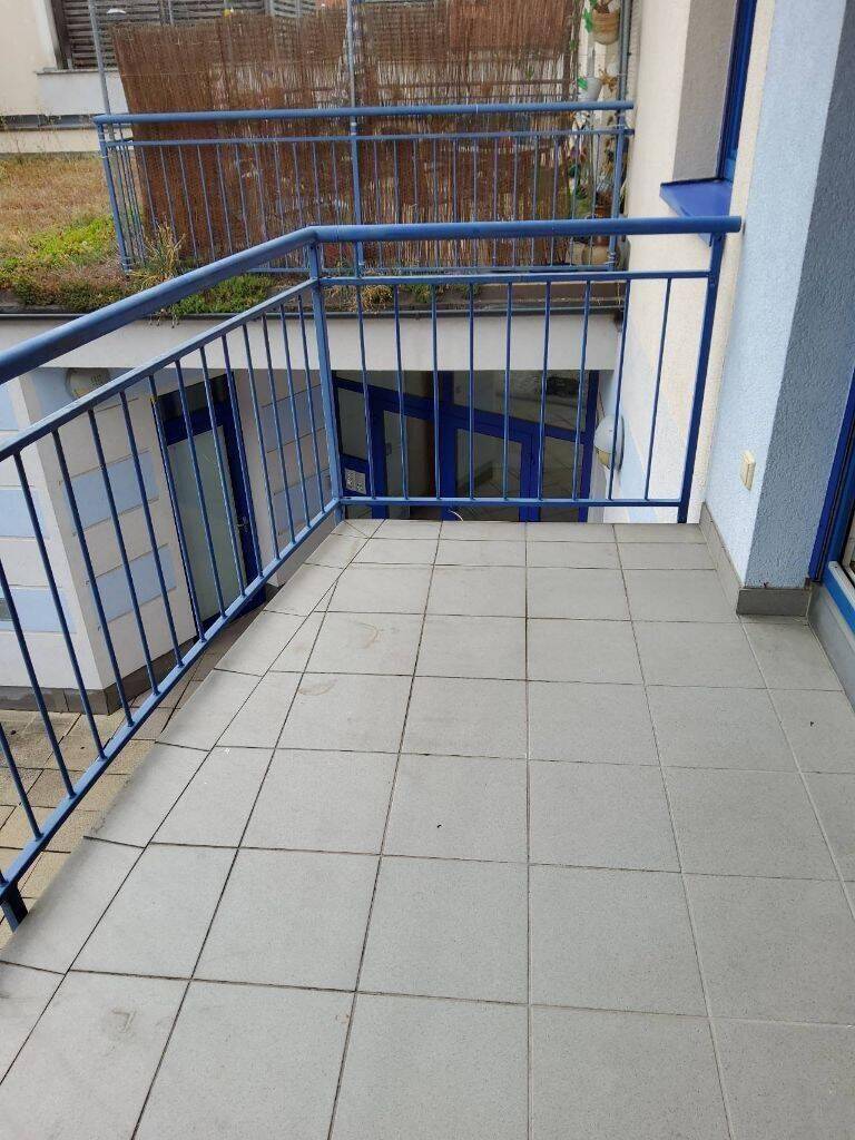 Balkon mit blauen Geländern und Fliesenboden, Blick auf einen tiefer gelegenen Bereich.