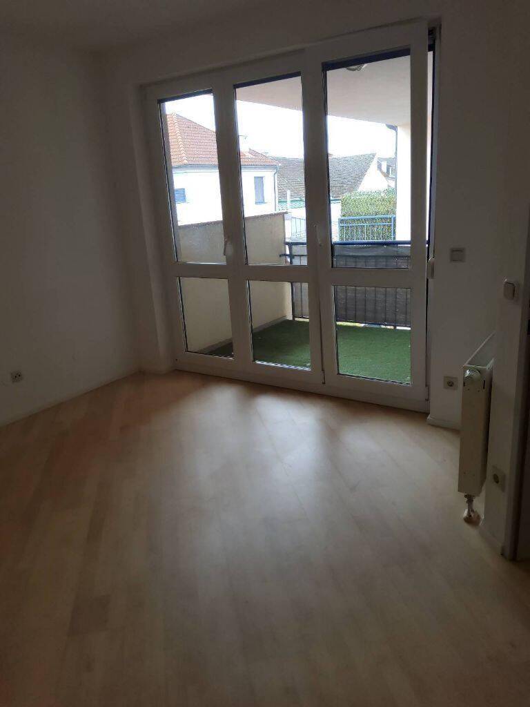 Heller Wohnraum mit Zugang zu einem kleinen Balkon und hellem Holzboden.