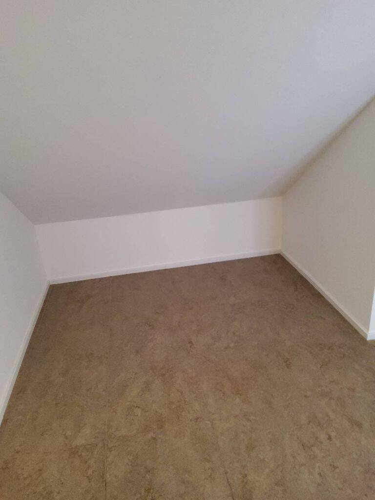 Leerer Raum mit Dachschräge und braunem Linoleumboden, bereit zur individuellen Gestaltung.