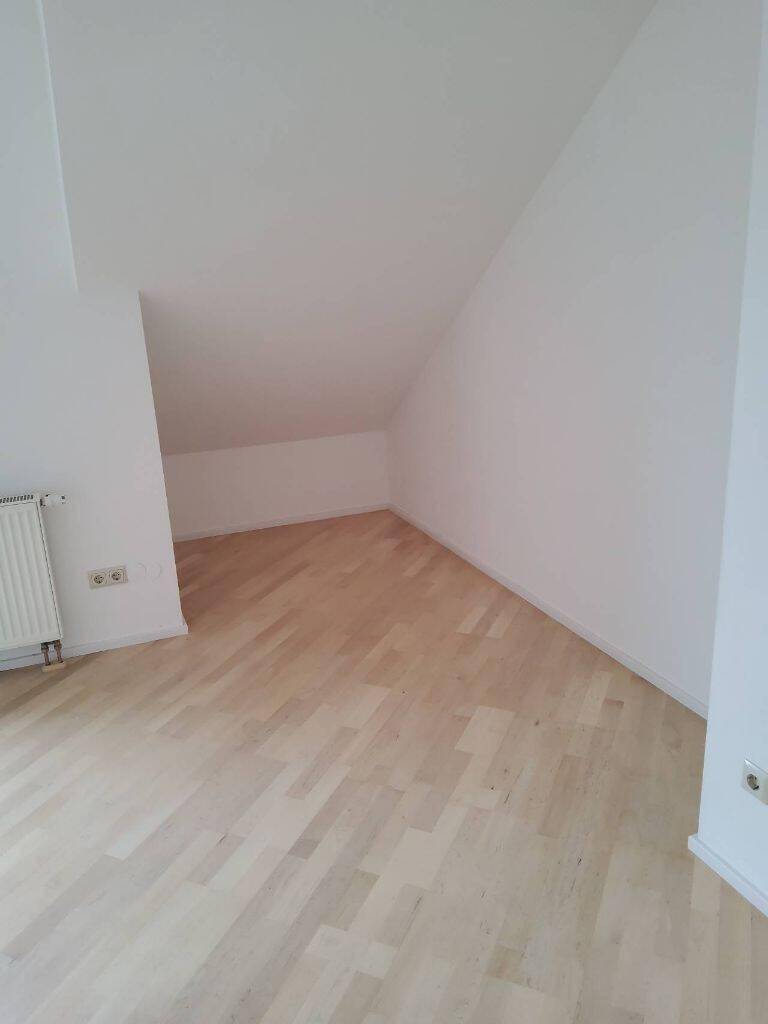 Geräumiger Raum mit Dachschräge, hellem Holzboden und Heizkörper, ideal als Schlafzimmer.