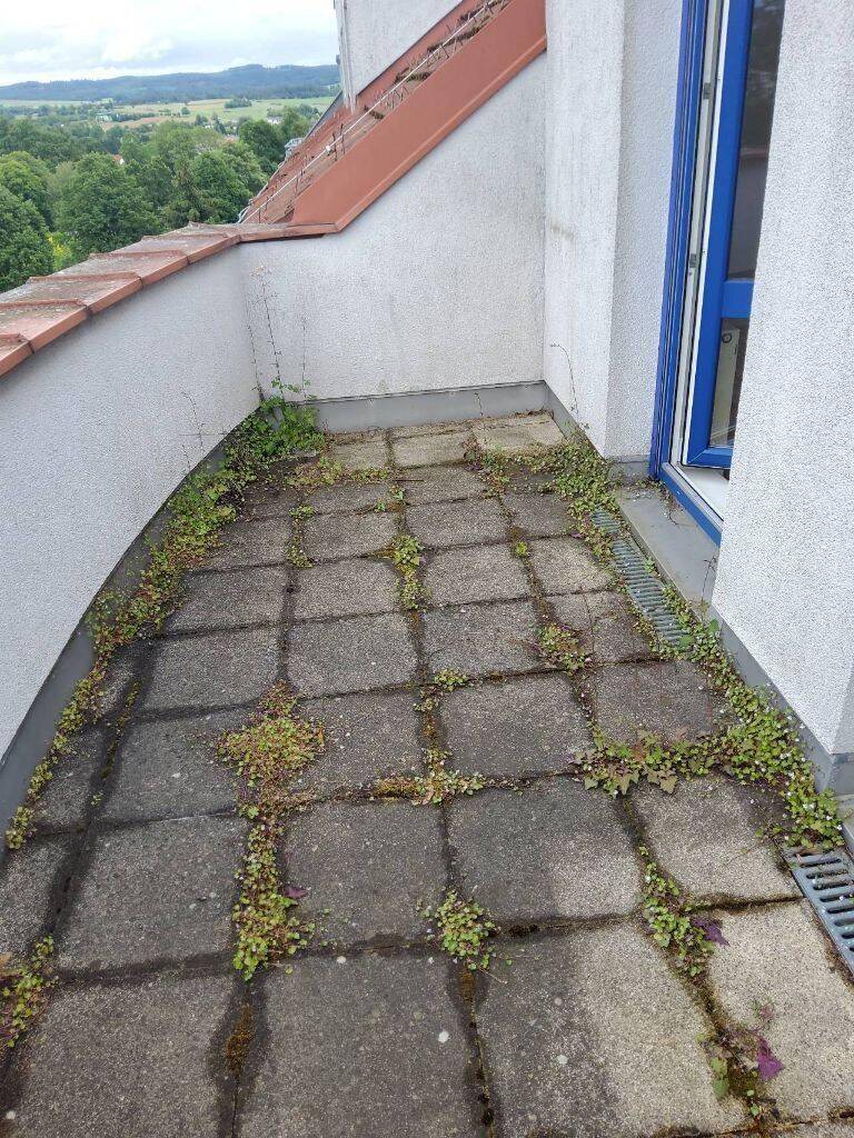 Ungepflegter Balkon mit Betonplatten und Blick auf die grüne Landschaft.