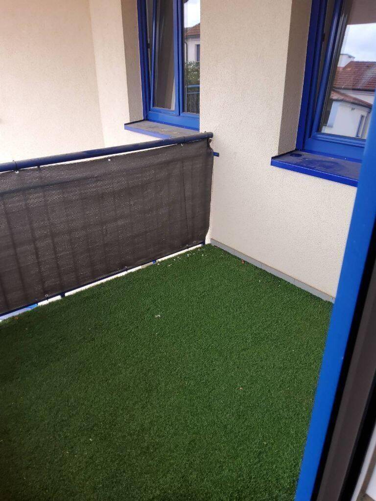 Kleiner Balkon mit Kunstrasen und blauen Fensterrahmen, ideal für eine gemütliche Sitzecke.