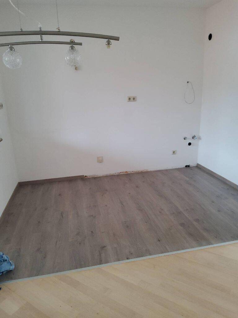 Leerer Raum mit Laminatboden und Anschlüssen für eine mögliche Küchenzeile oder Waschküche.