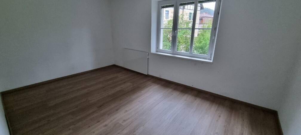 Leerer Raum mit Laminatboden, Heizkörper unter dem Fenster und weißen Wänden, bereit zum Einzug.