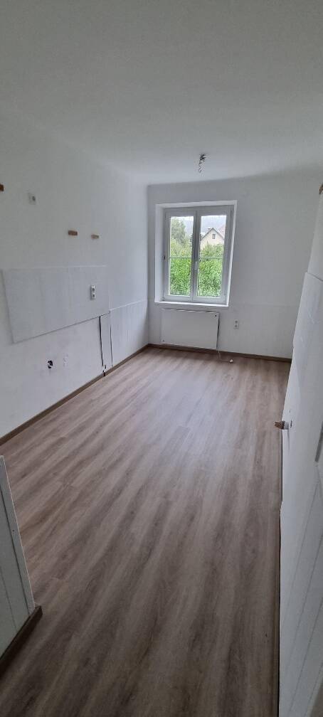 Leerer Raum mit Laminatboden, weißen Wänden und einem Fenster, das viel Tageslicht hereinlässt.