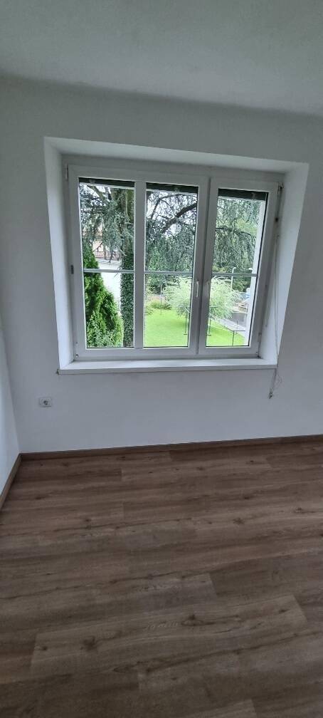 Detailaufnahme eines Fensters in einem leeren Raum mit Laminatboden und Blick auf den Garten.
