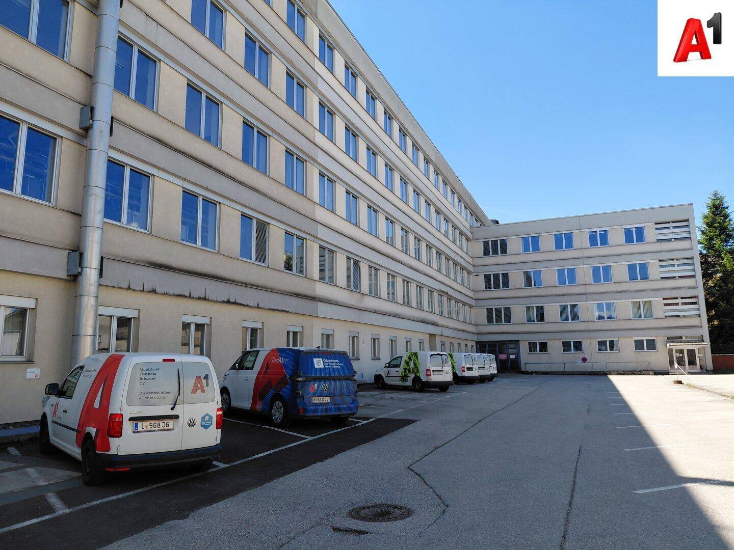 Ansicht des Bürogebäudes von der Seite mit Parkplätzen und Firmenfahrzeugen.