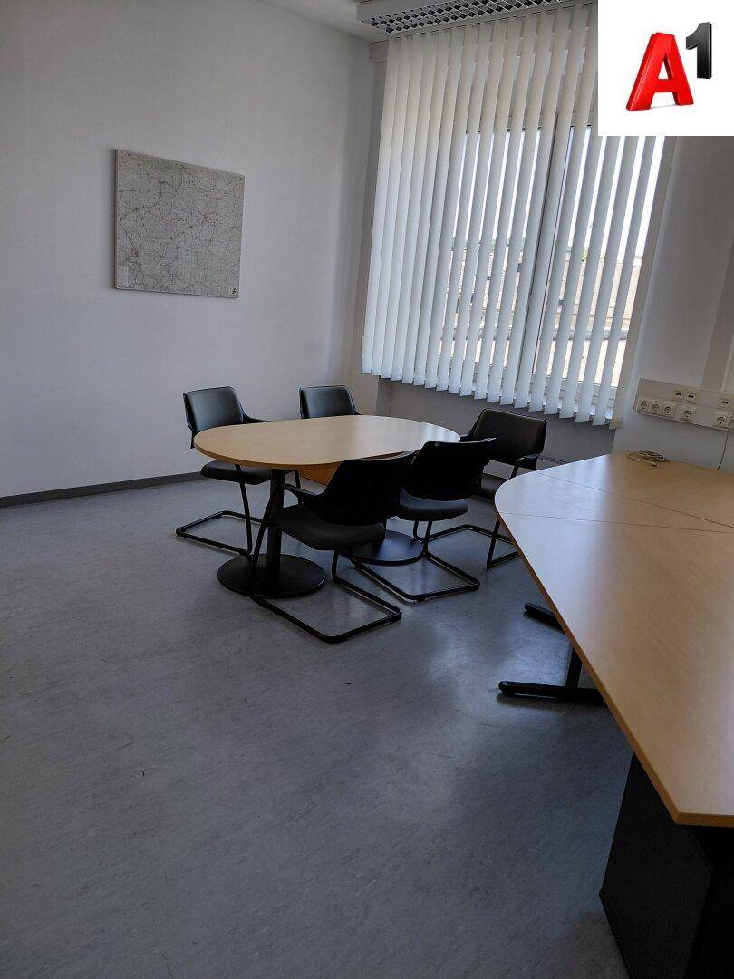 Kleiner Besprechungsbereich in einem Büro mit rundem Holztisch und schwarzen Stühlen.