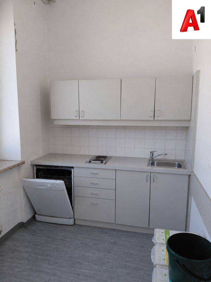 Kleine Küchenzeile mit weißen Schränken, Spüle, Kochfeld und integriertem Geschirrspüler.