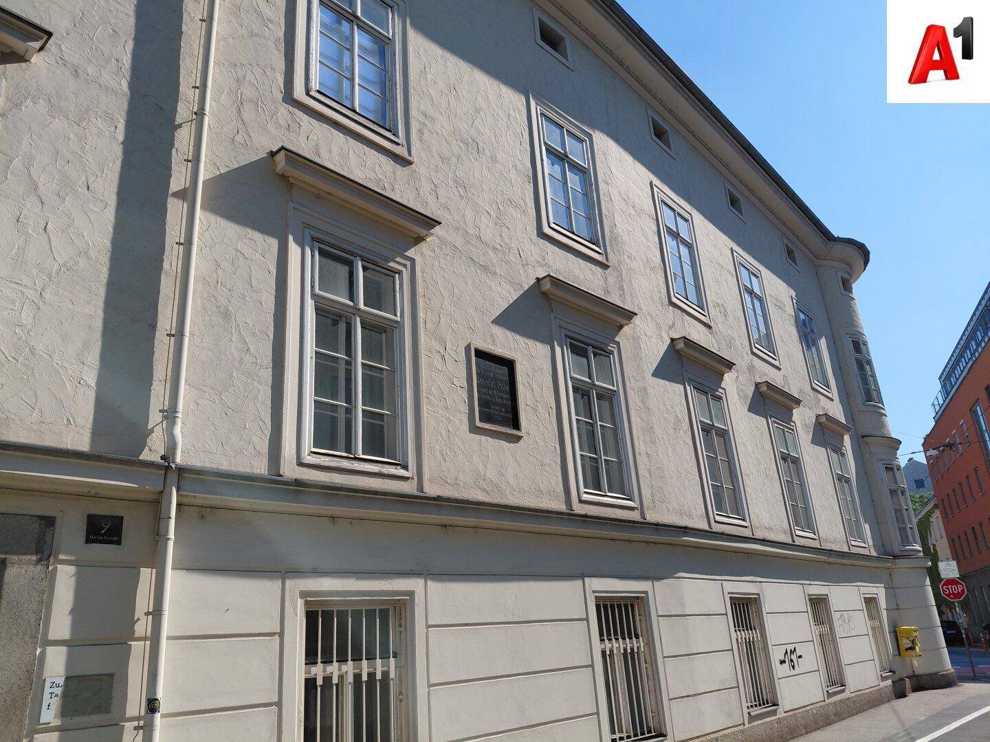 Detaillierte Außenansicht des Gebäudes mit verzierten Fenstern und einer Gedenktafel an der Fassade.