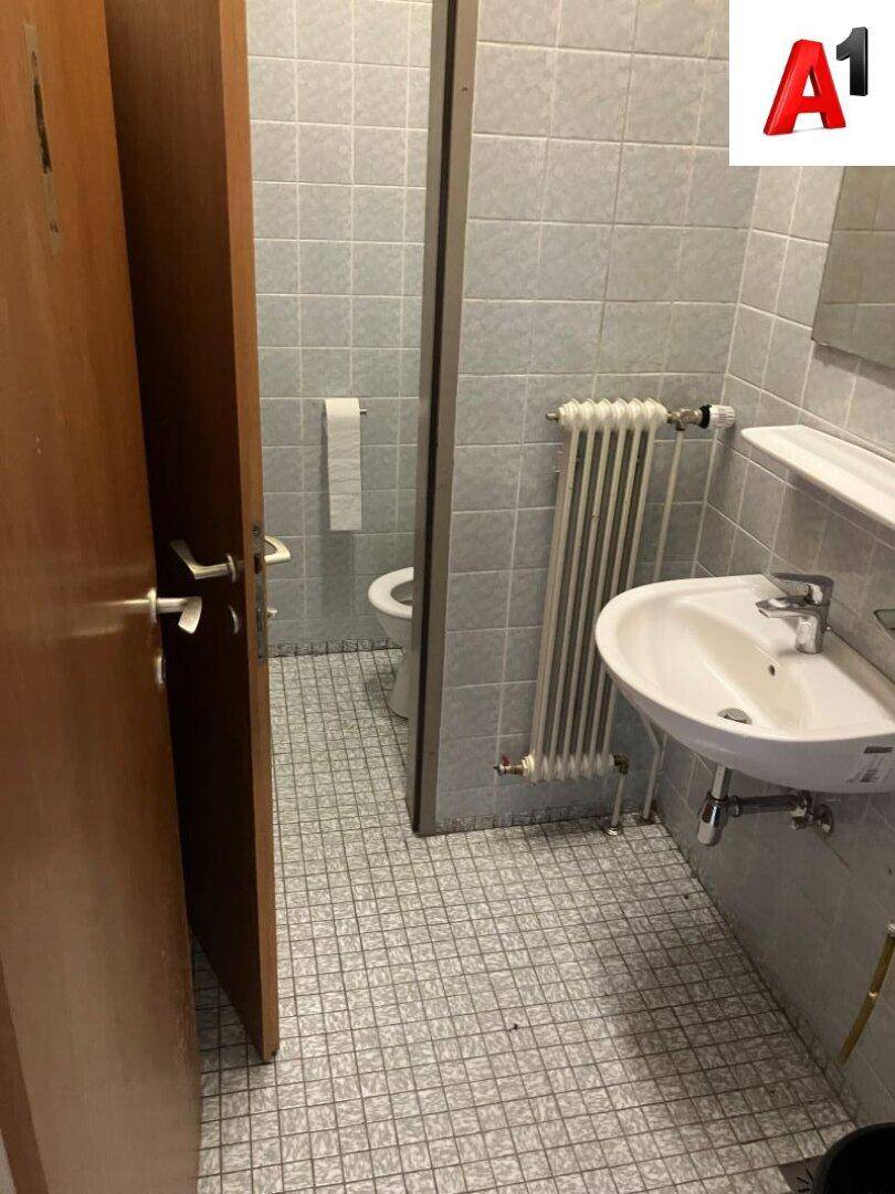 Kleiner Toilettenraum mit grauen Fliesen, Waschbecken und Heizkörper.