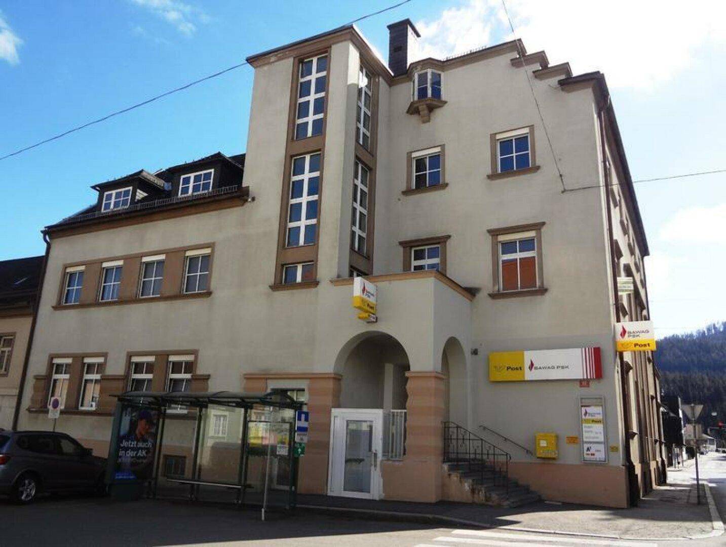 Historisches Gebäude mit beiger Fassade, Rollläden und Blick auf die umliegenden Berge, beherbergt eine Postfiliale.
