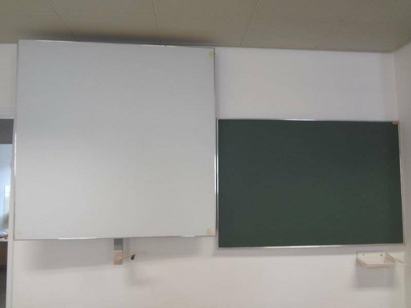 Nahaufnahme einer weißen Tafel und einer grünen Kreidetafel an einer hellen Wand in einem Raum.